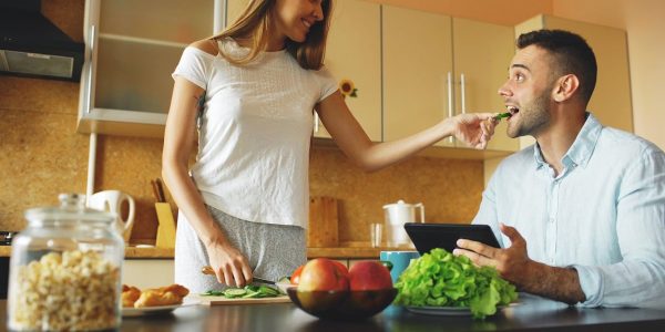 Attractive couple chatting in the kitchen early morning. Beautiful woman feed her husband while cooking breakfast at home