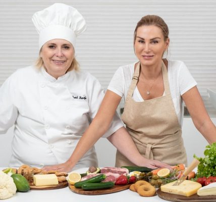 Two female chefs with variety of fresh ingredients in a kitchen setting, showcasing culinary preparation.