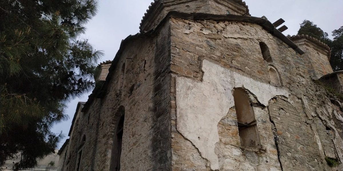 Low-angle view of an ancient stone building in Samos, Greece, surrounded by greenery.